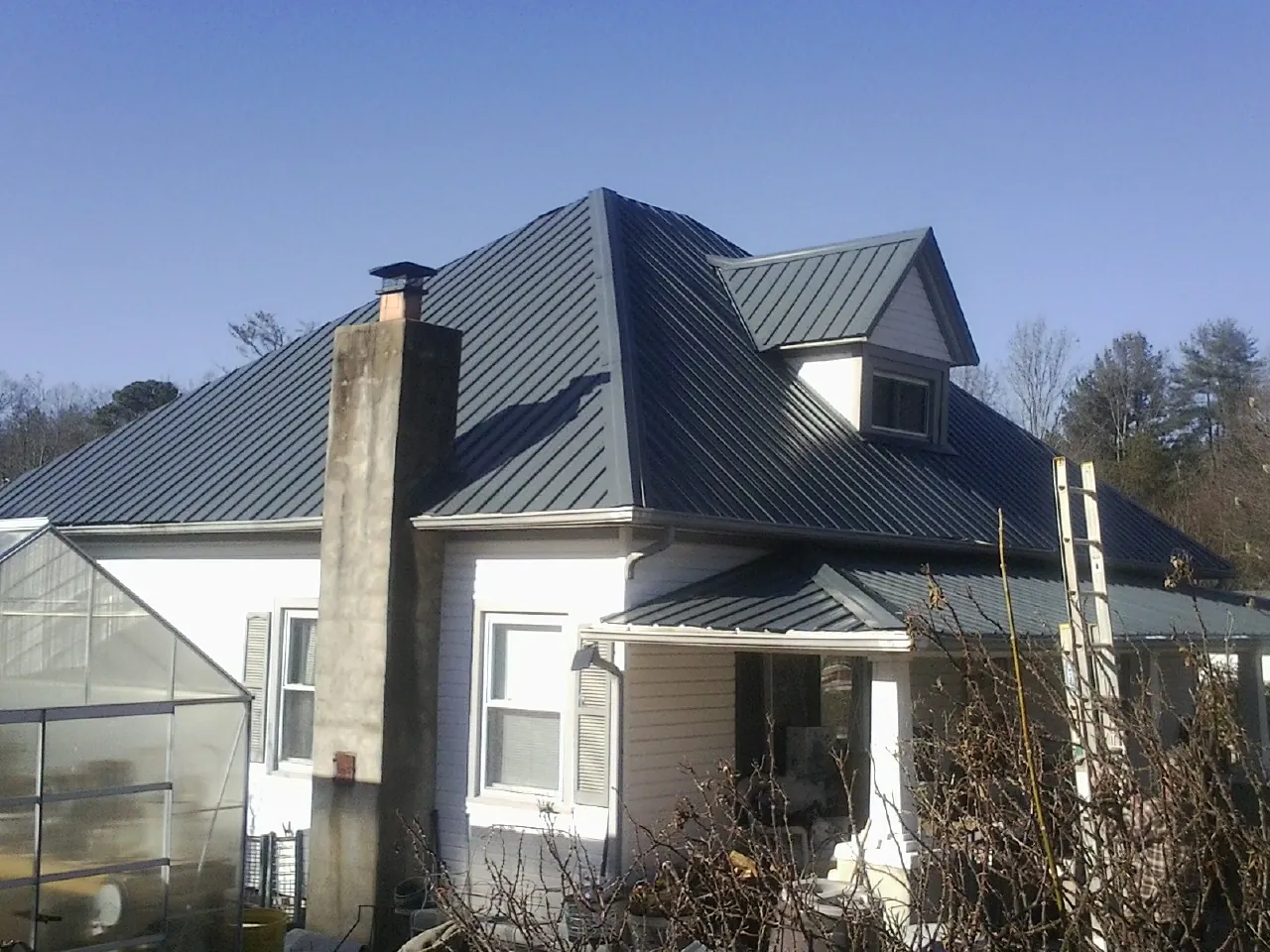 Dark blue standing seam metal roof on a white farmhouse with dormer — Slate & Tile Roof Repair by Roofing Brothers in Thicket