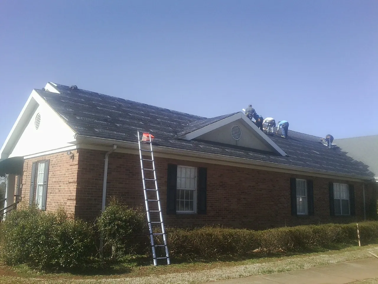 Crew tearing shingles off a brick ranch roof with a ladder set — Emergency Roof Repair work by our crew in Thicket