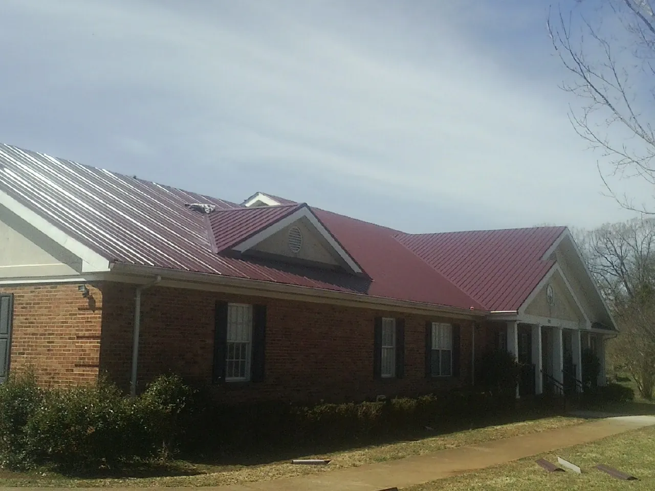 Red metal roof with gabled entries on a long brick building, from a Hail Damage Roof Repair job in Thicket