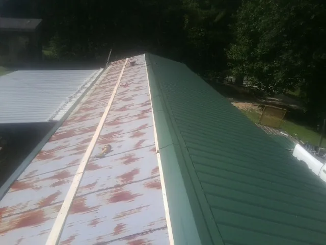 Old rusted panels beside newly installed green metal roofing — Wind Damage Roof Repair by Roofing Brothers in Thicket