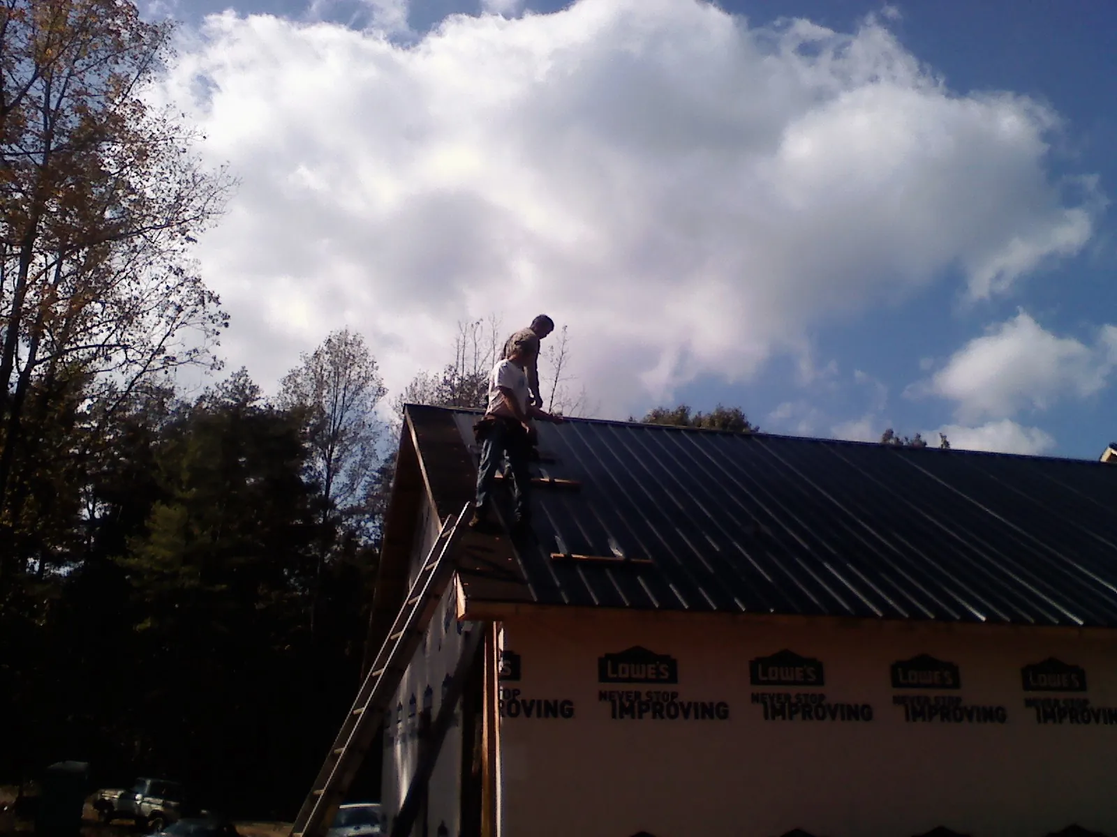 Roofer fastening dark metal panels high against a cloudy sky, from a Roof Inspection job in Thicket