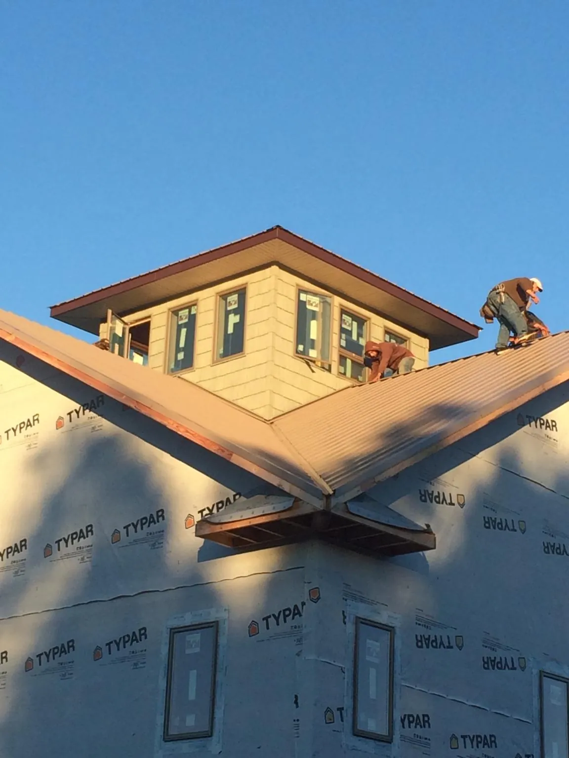 Roofers working around a rooftop cupola on a new metal roof at sunset — Roof Waterproofing in Thicket by Roofing Brothers